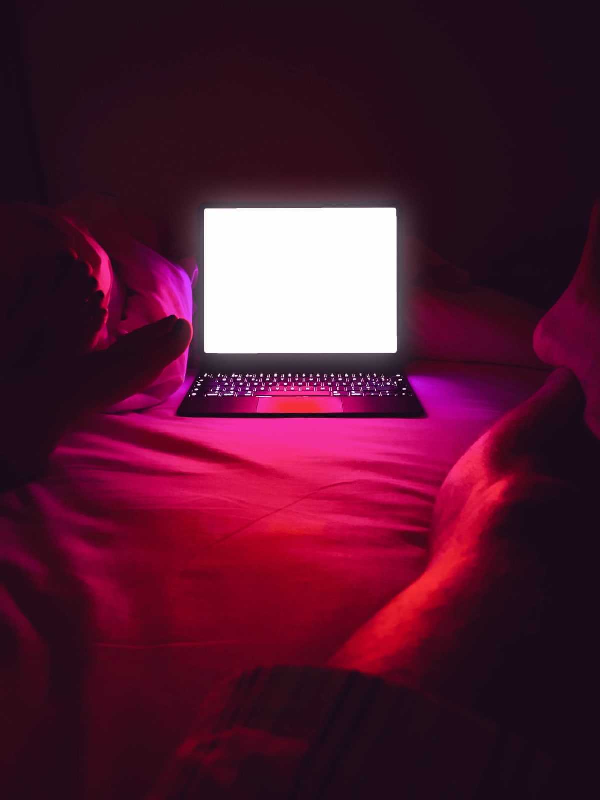 Adult couple watching series online in streaming platform bringin cinema at home, picture taken from personal perspective with legs and bright screen illuminating the bedroom with red light.