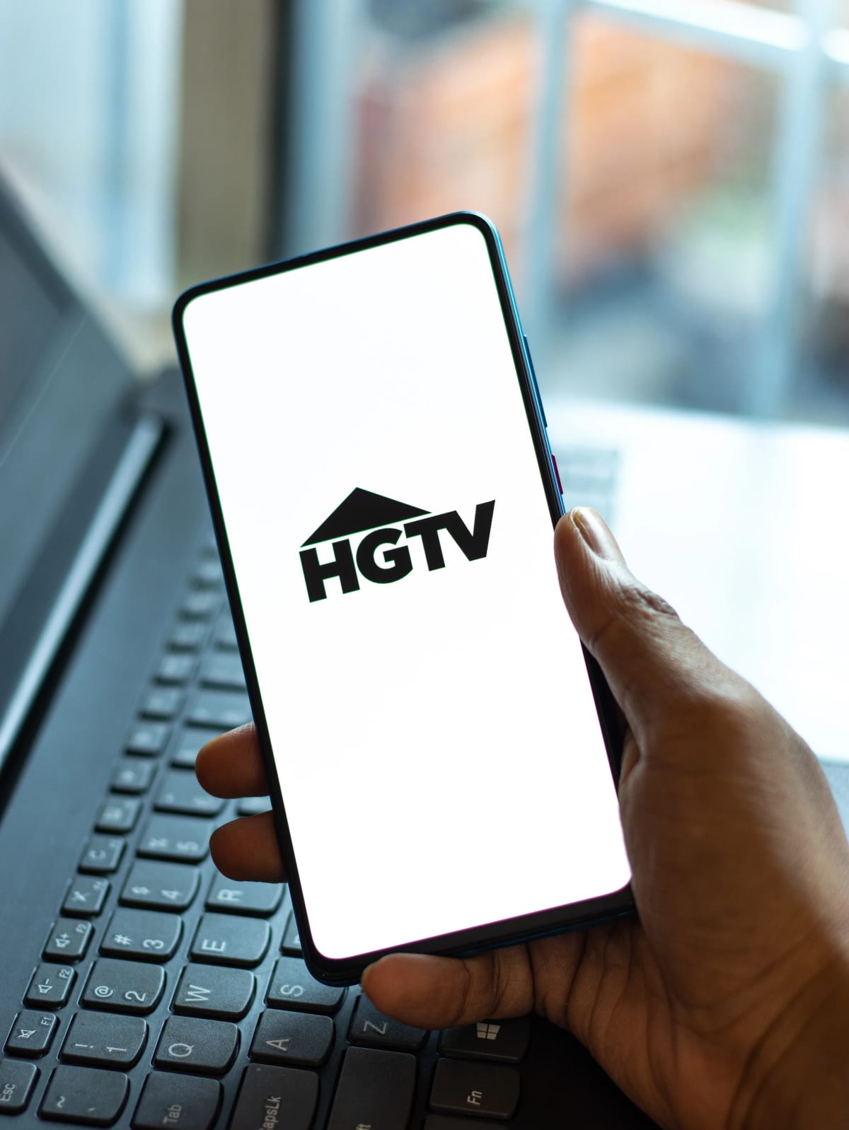 HGTV logo on a phone, being handheld over a computer keyboard