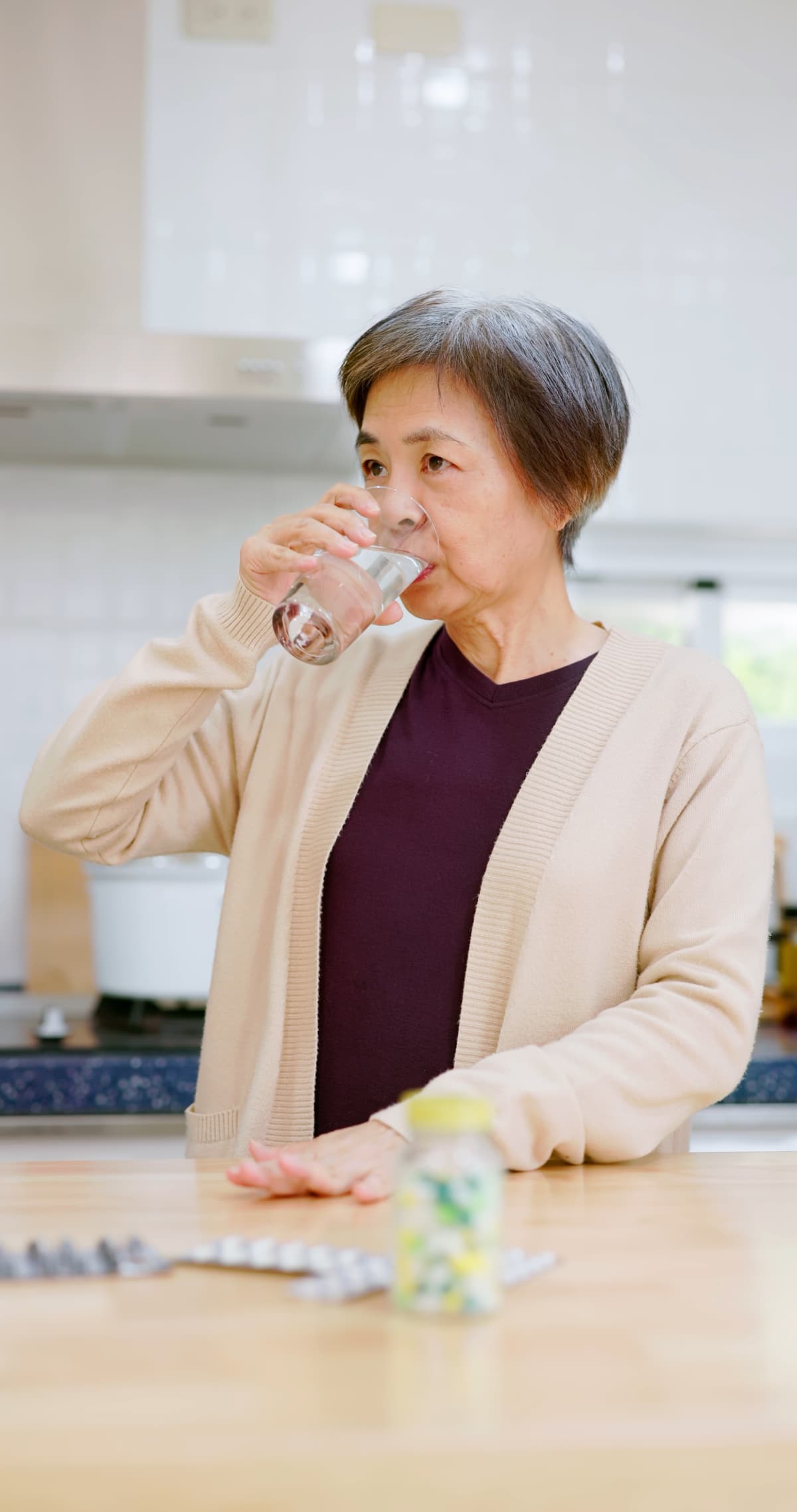 asian elderly woman take medicine with a glass of water in kitchen at home