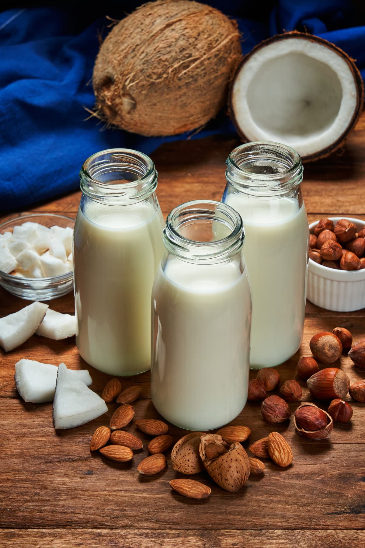 Various organic vegan plant based milk in glasses and glass bottle and ingredients (nuts, oatmeal) on beige background. Non Dairy milk substitute drink, healthy eating. Lactose-free milk in minimal style, copy space.