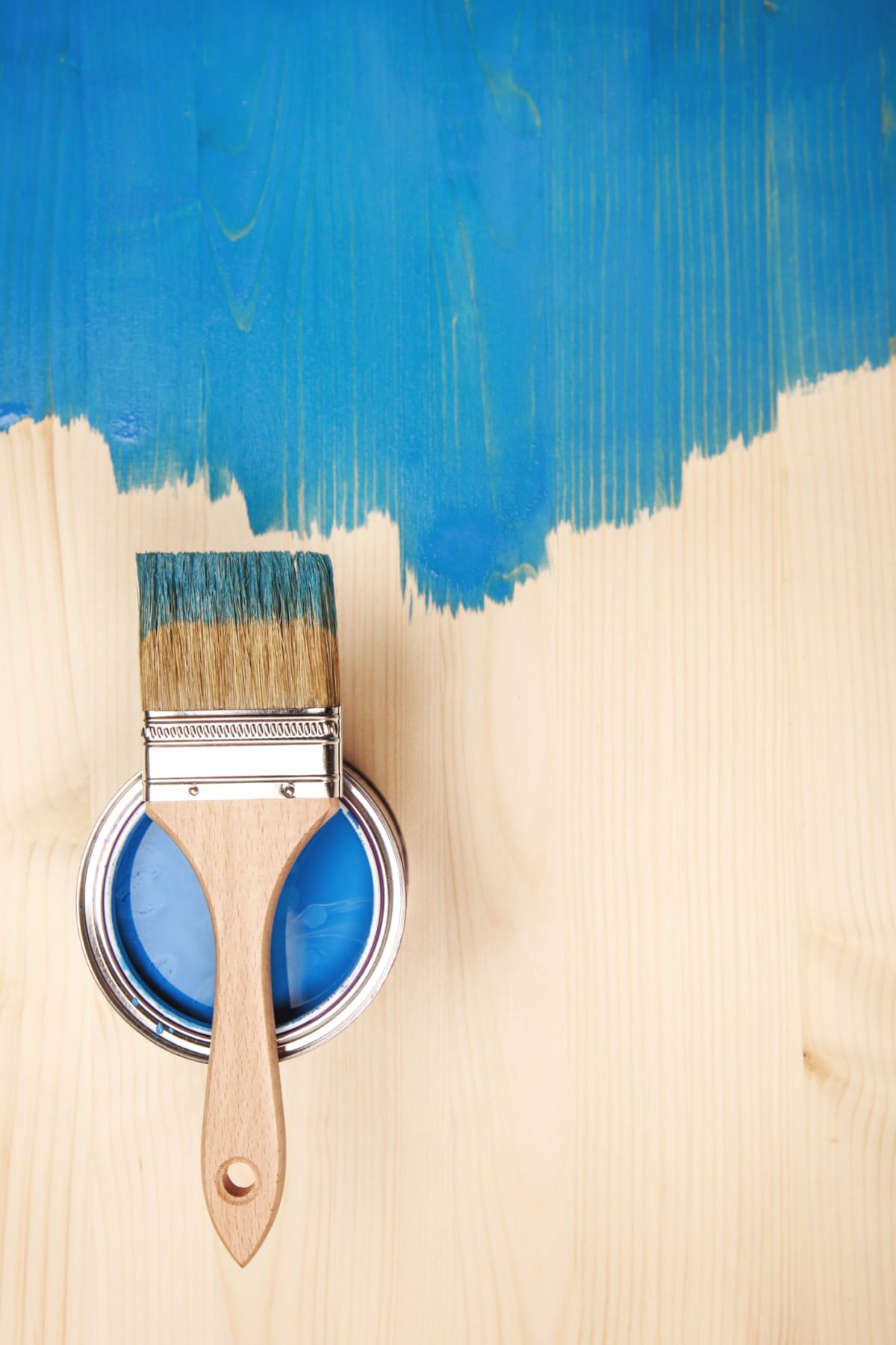 Paint brush on the can lying on wooden background. The surface is half - toned with blue color.