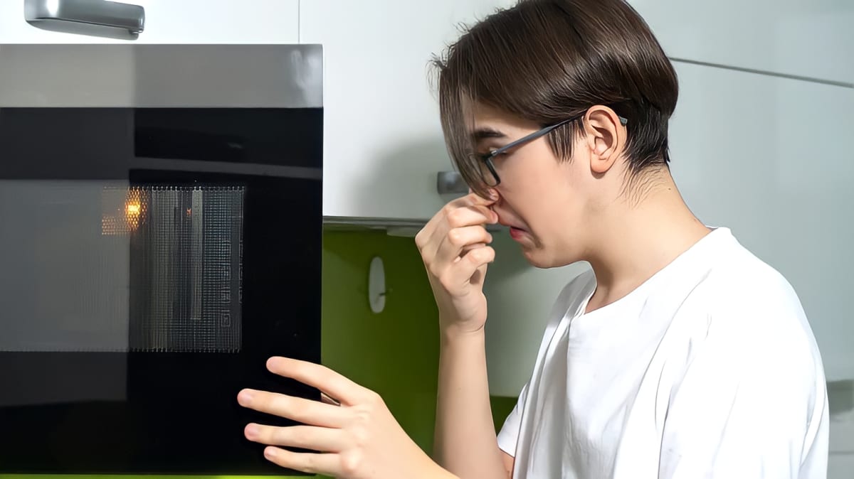 A person holding their nose while opening a microwave