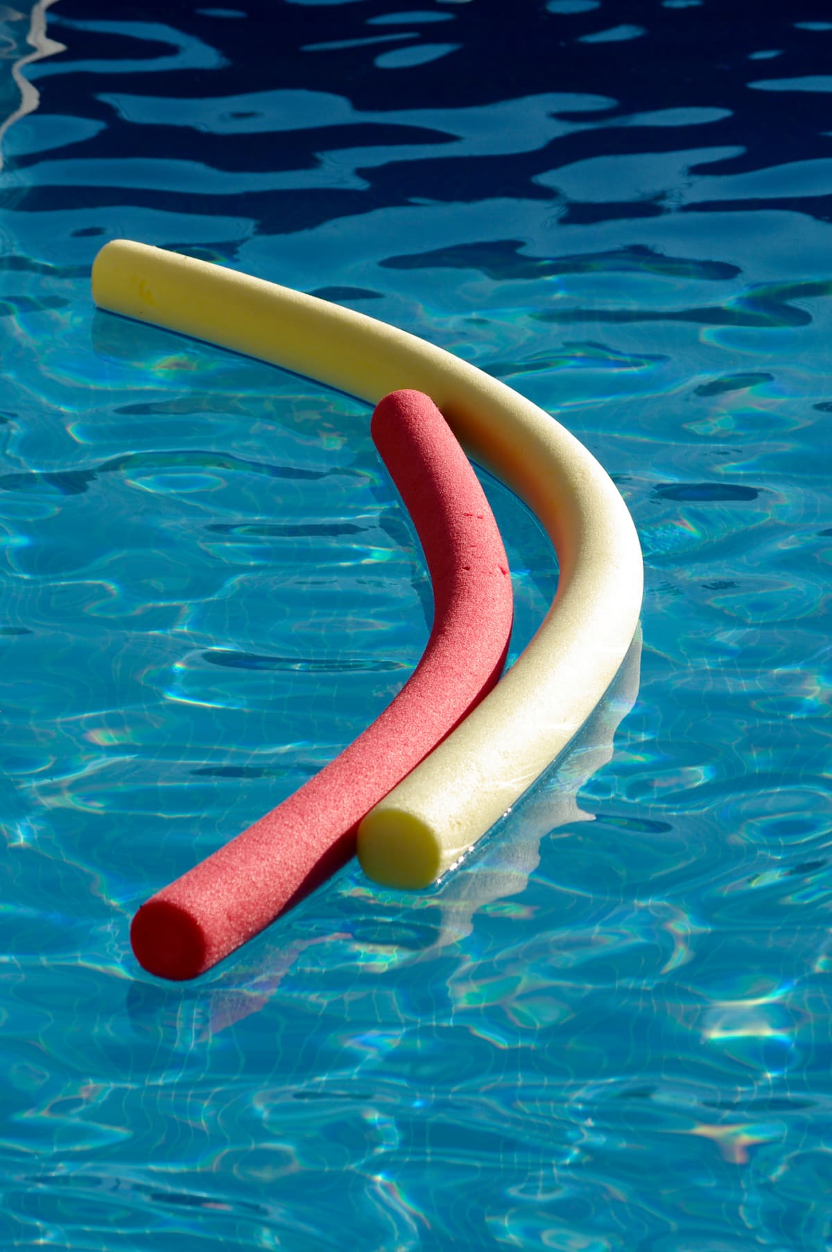 Colorful pool noodles floating in a sunlit swimming pool