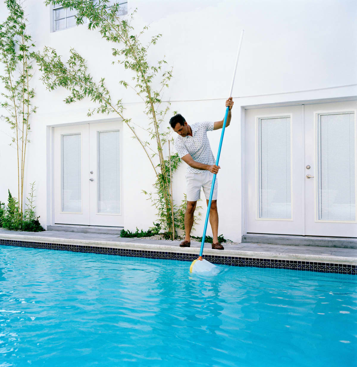 A man cleaning a pool with a telescopic pole