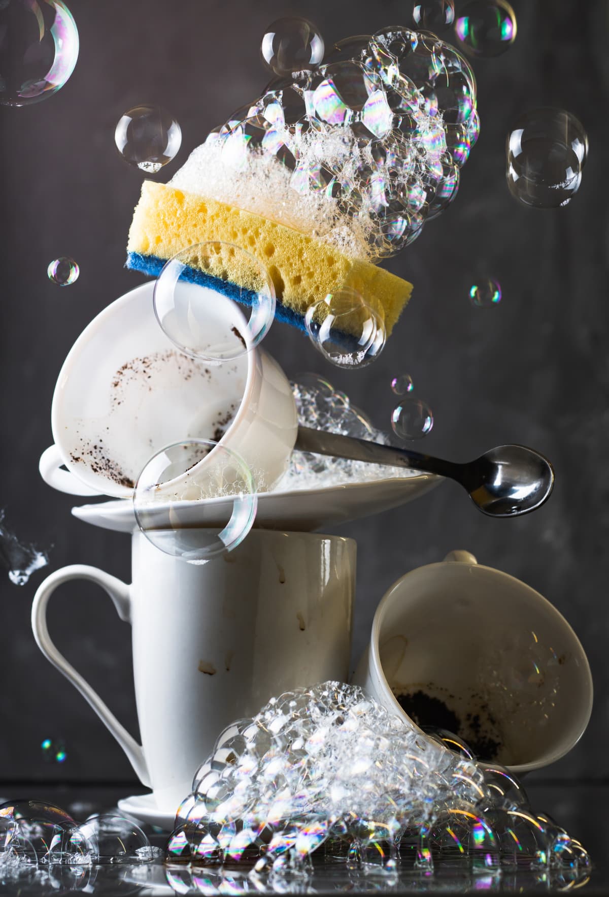 Stack of dirty white dishes on dark background, with washing sponge and bubbles