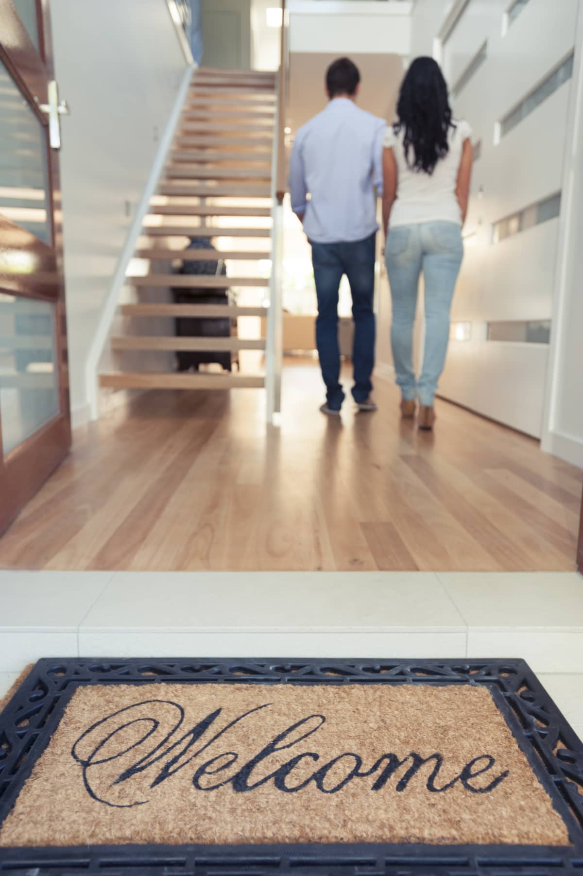 Young couple walking into their new house with a welcome mat at the front door