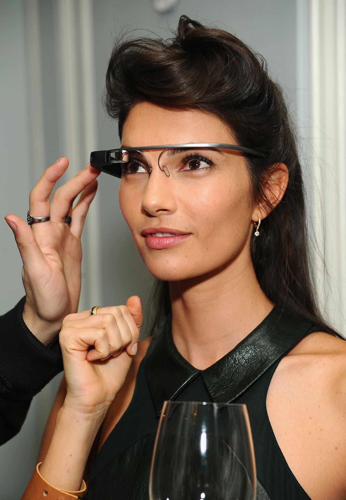 Woman wearing the Google Glass on her face as a man's hand turns on the device