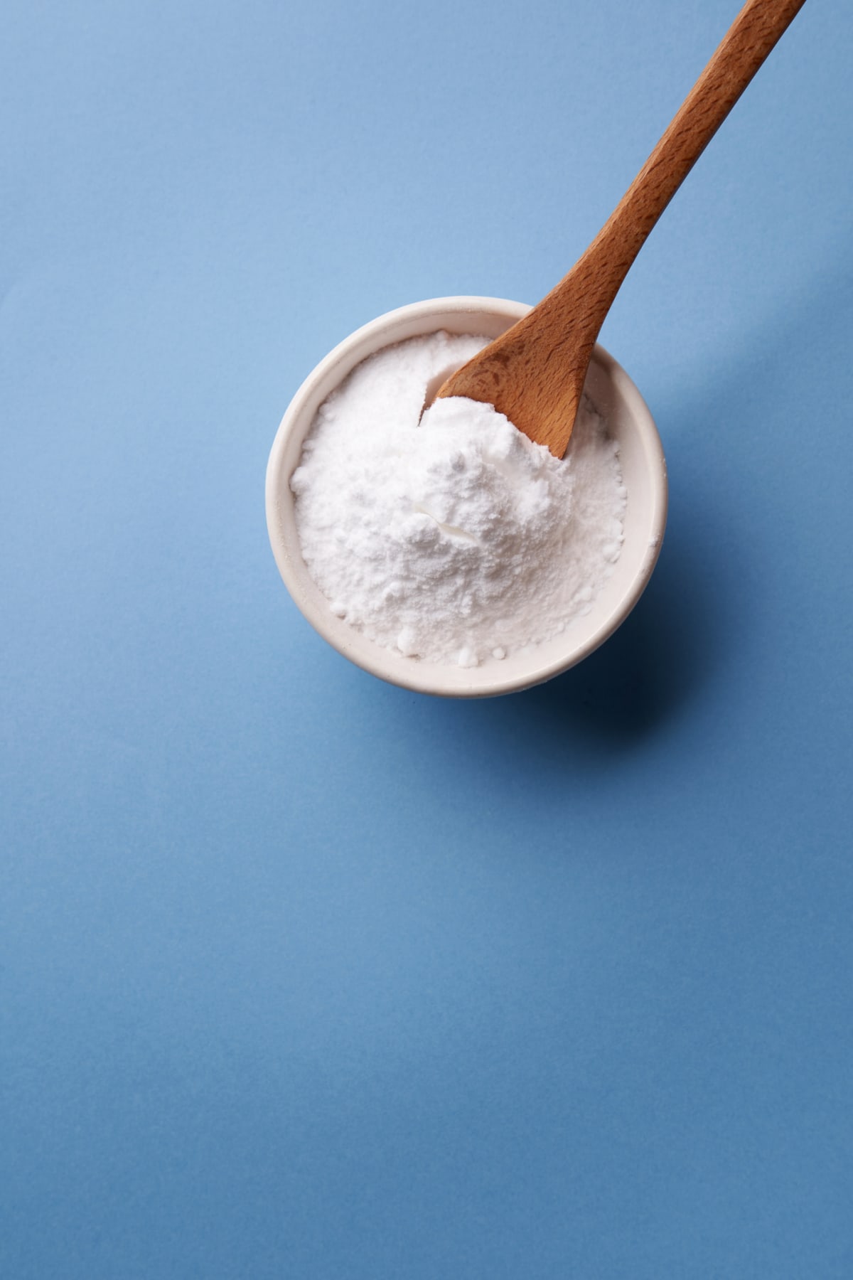 A spoon lifts baking soda from a small bowl, on a blue background