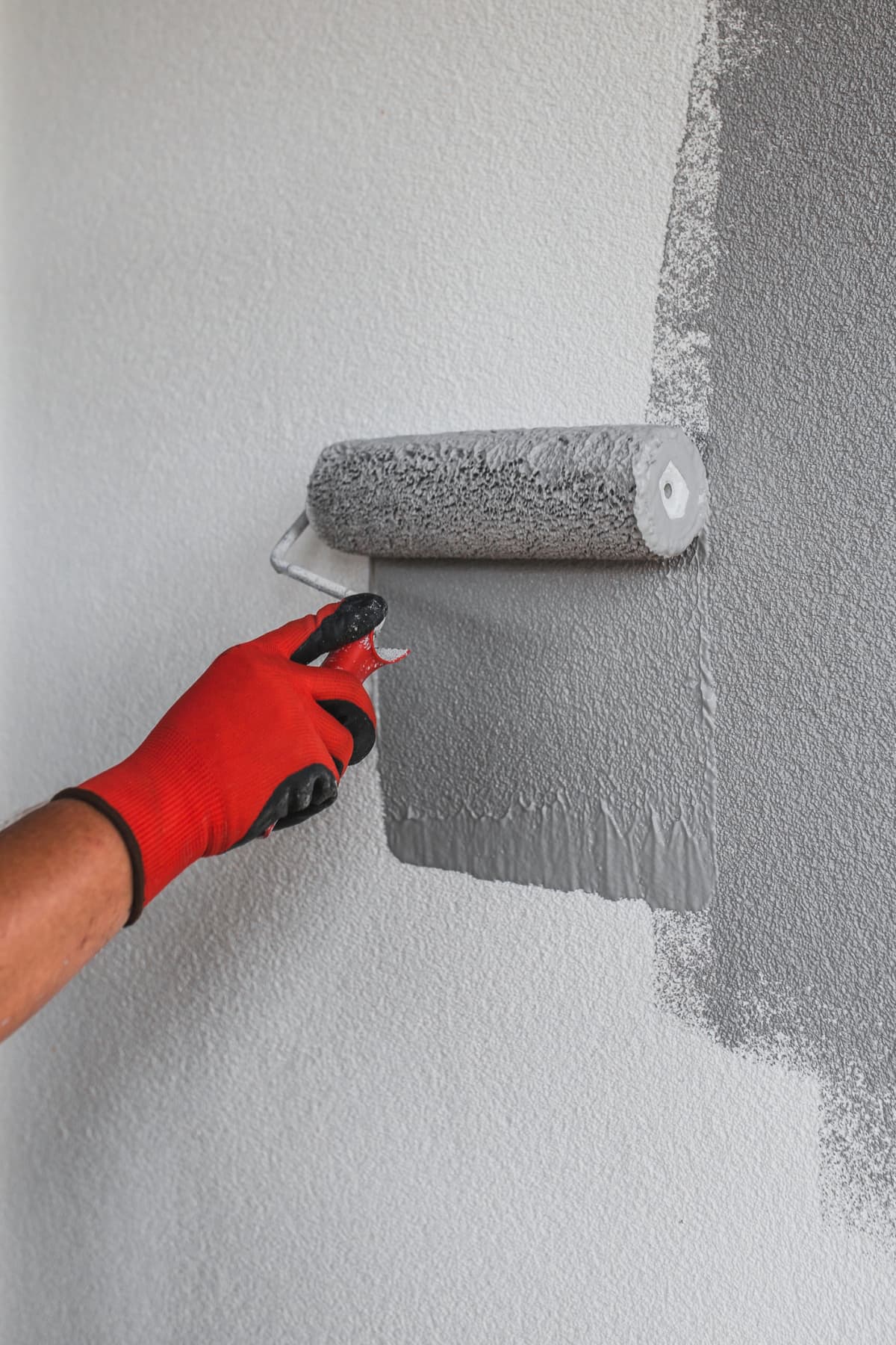 A person painting a wall with gray paint