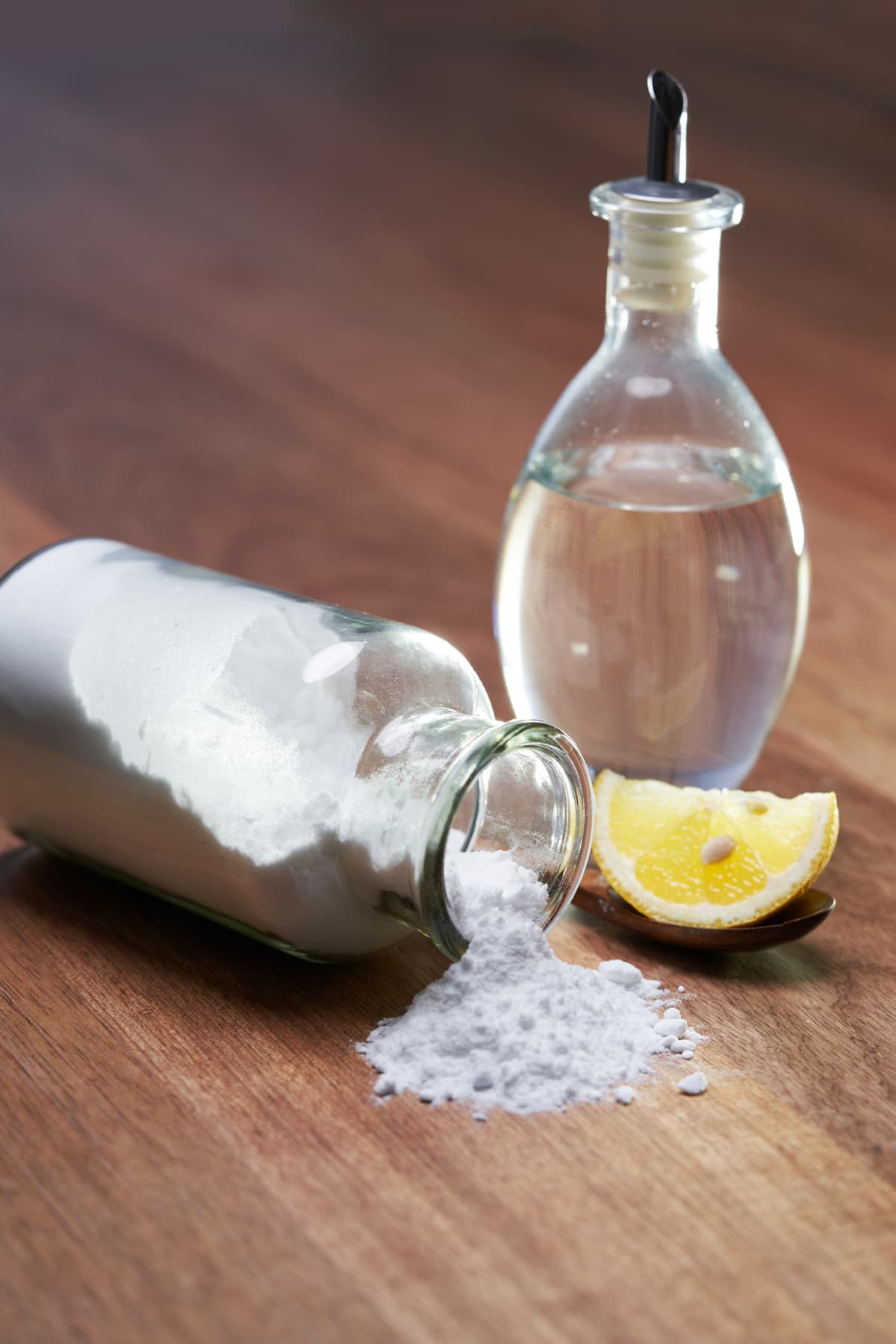 A bottle of white vinegar with baking soda and lemon on wooden table top