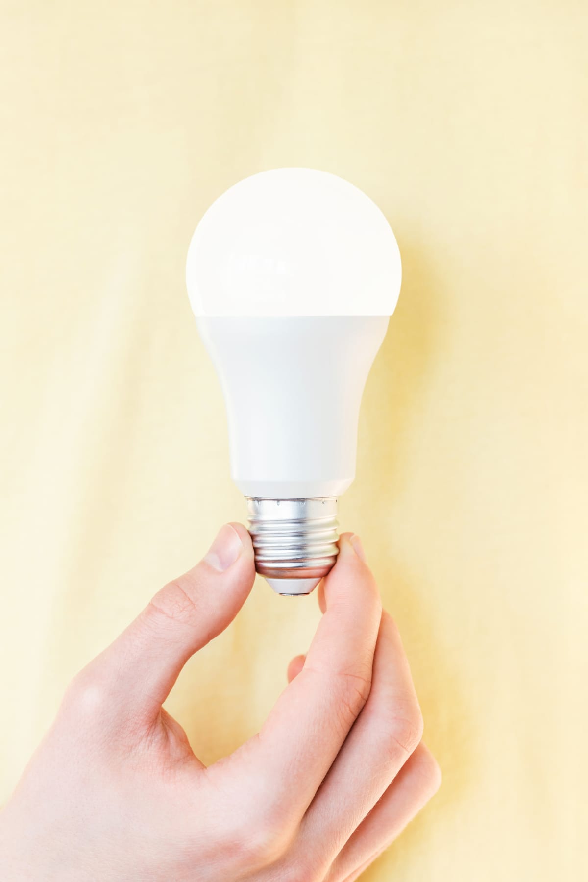 Hand holding shining LED light bulb against yellow background. Concept of responsible consumption of electricity or having an idea.