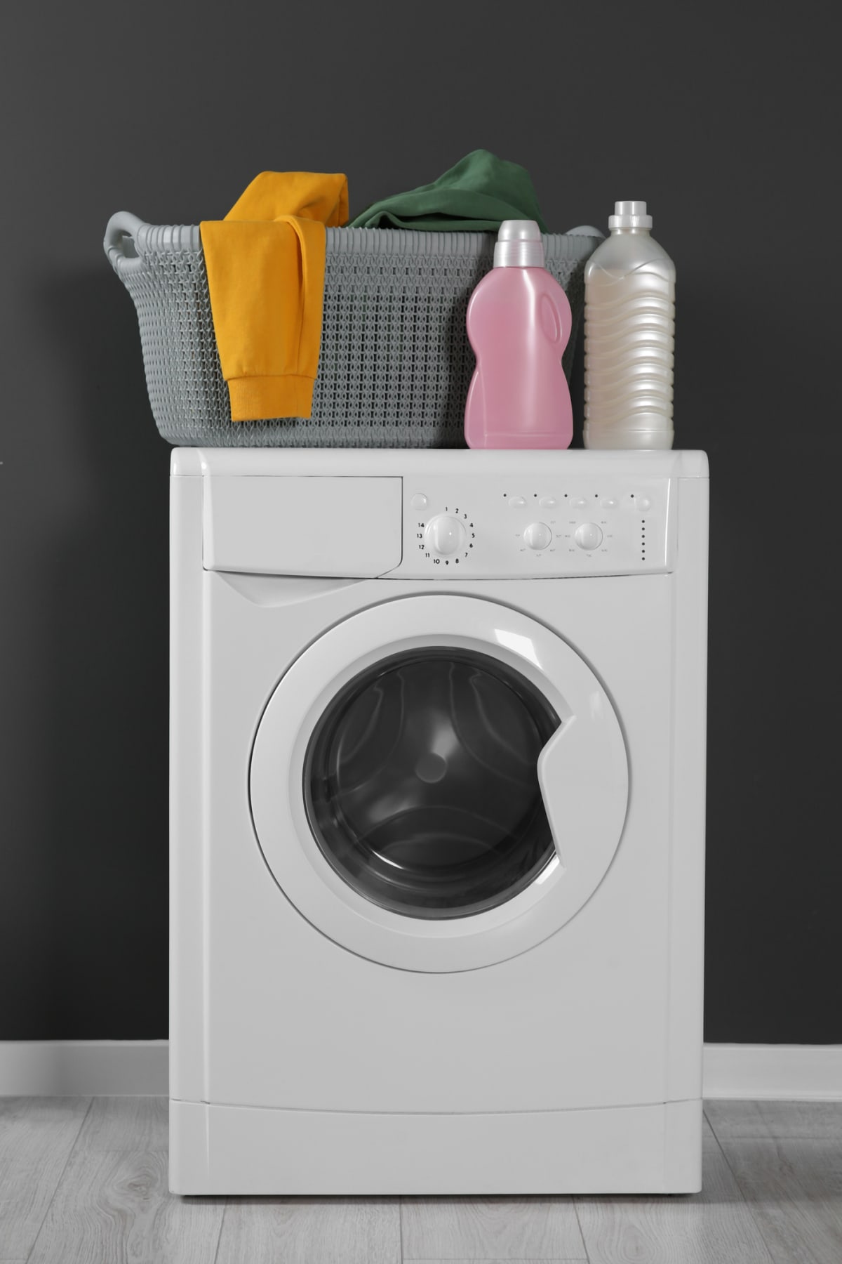 A laundry basket filled with clothes, a bottle of baby shampoo, and detergent, placed atop a washing machine