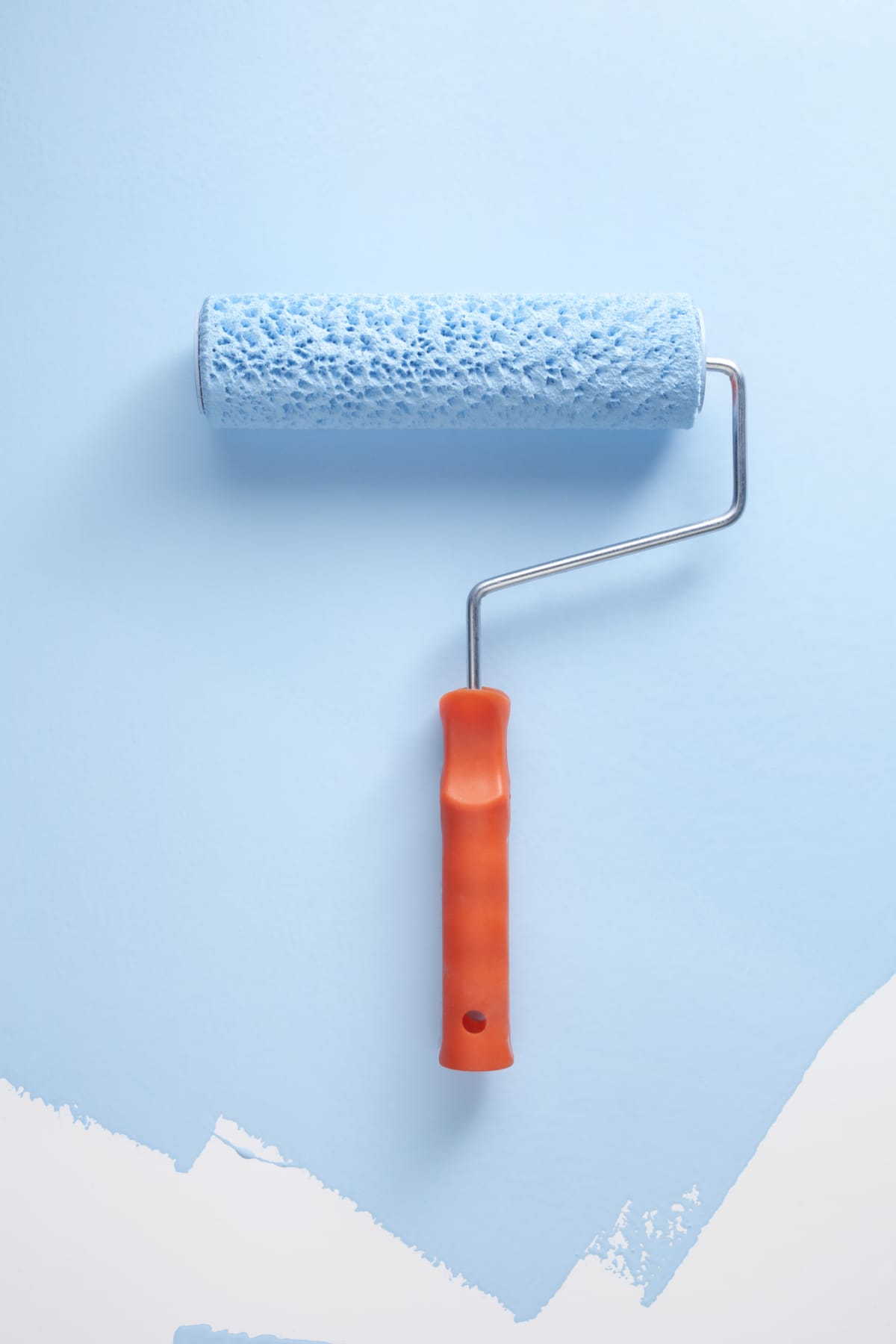 Paint roller painting a wall light blue