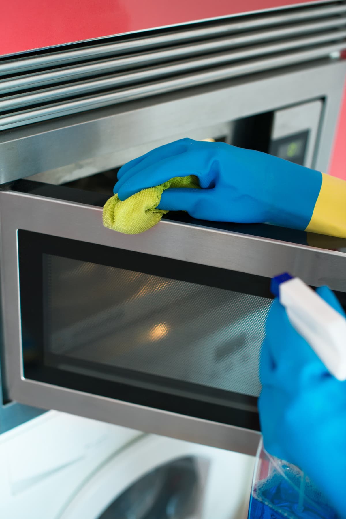 A woman wearing gloves wiping a microwave oven.
