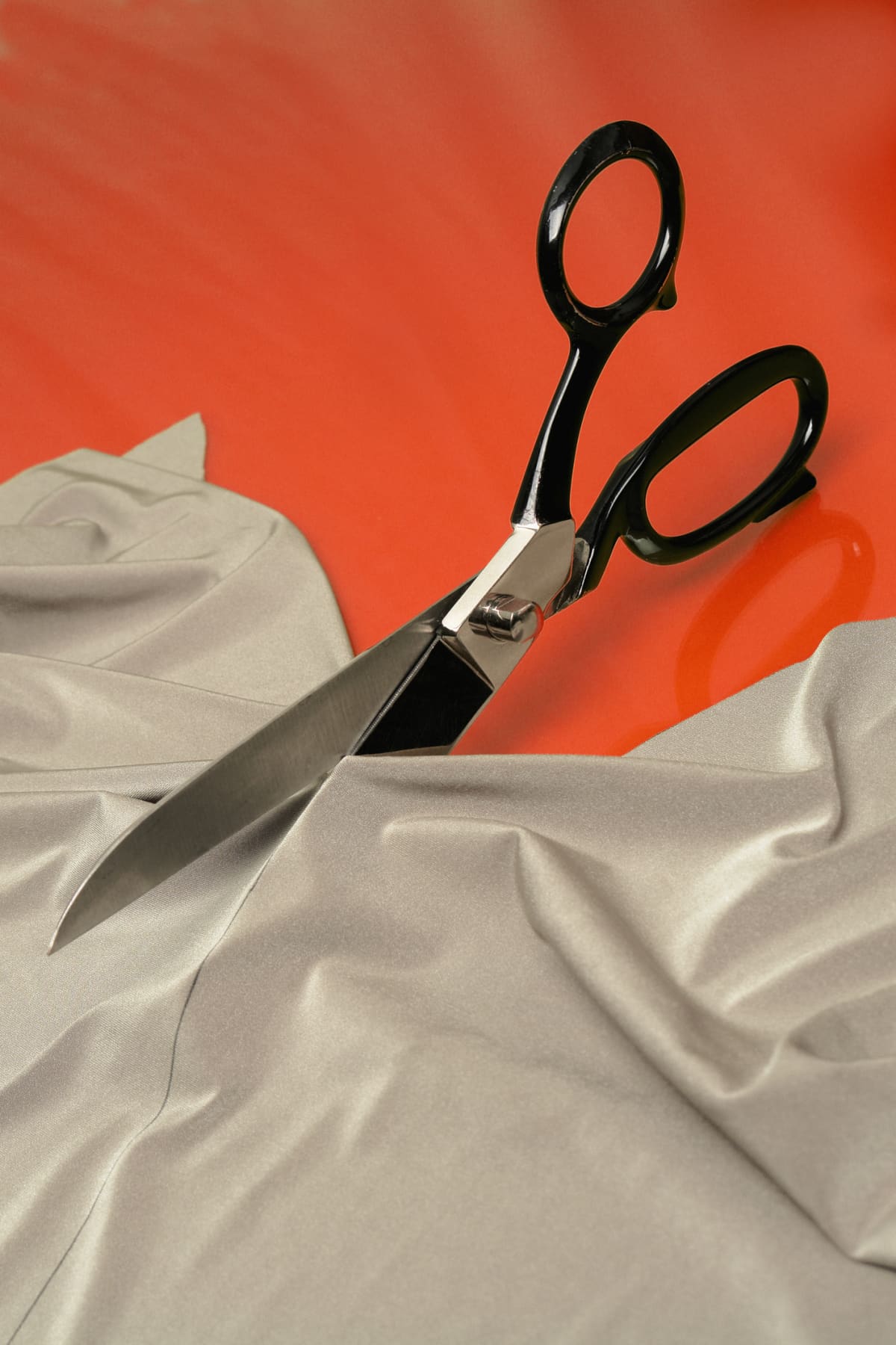 A pair of scissors cutting fabric against an orange background