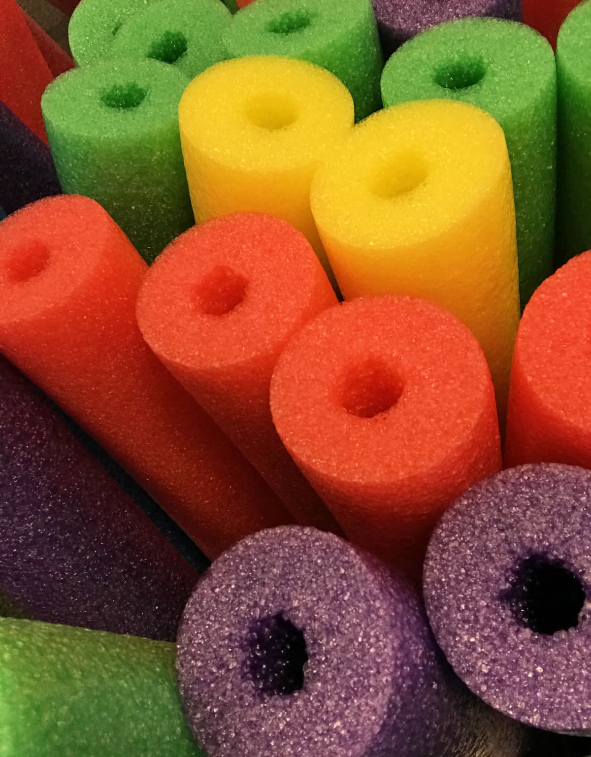 Assorted pool noodles in orange, yellow, green, and purple colors