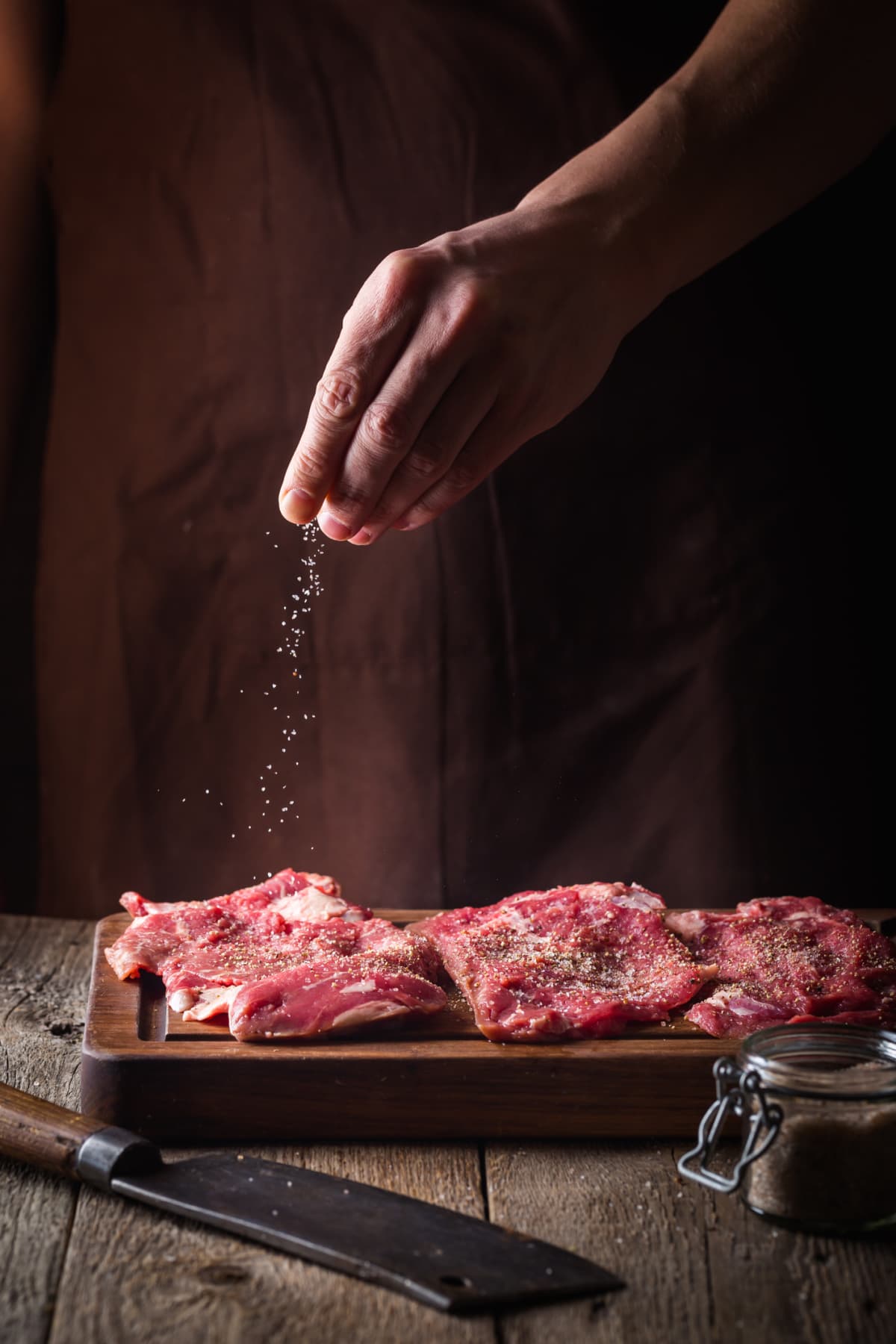 Hand seasoning meat with salt.