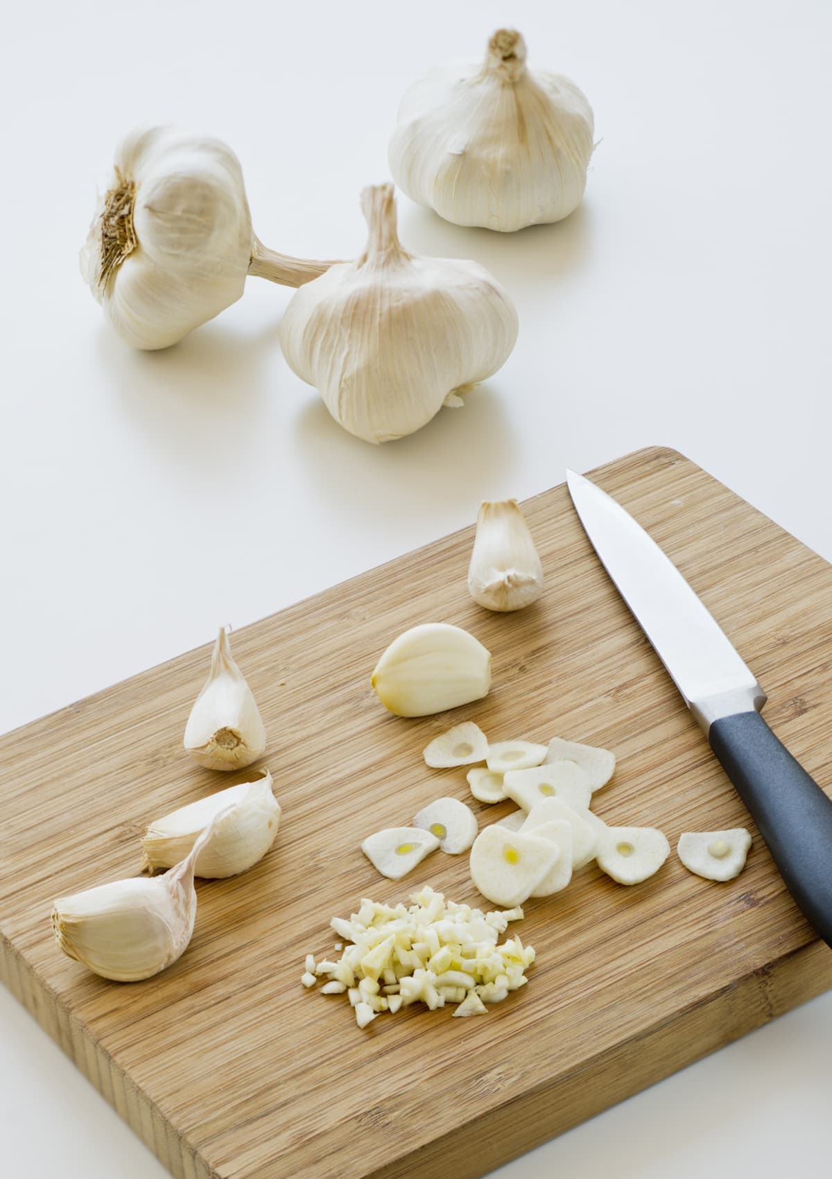 whole cloves of garlic next to individual cloves on a cutting board with knife