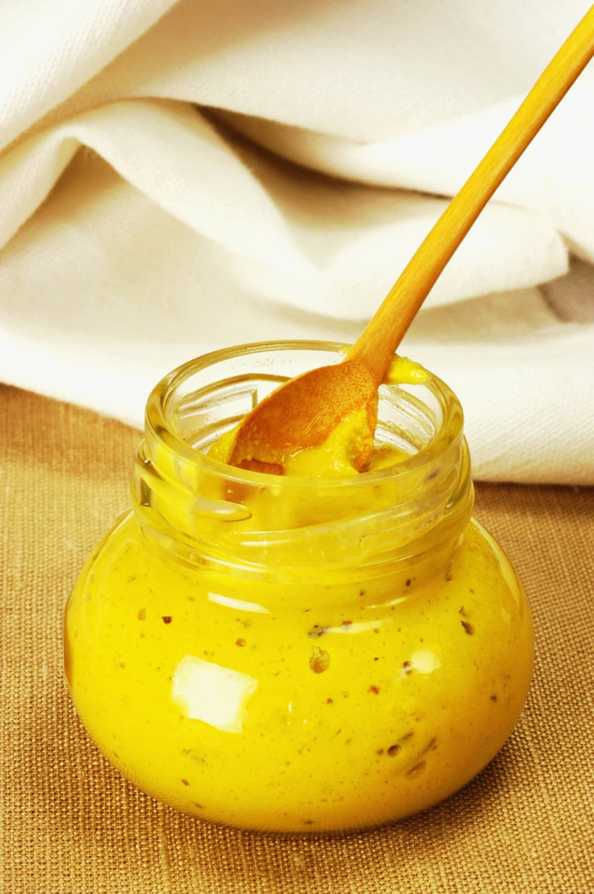 Glass jar of mustard with wooden spoon