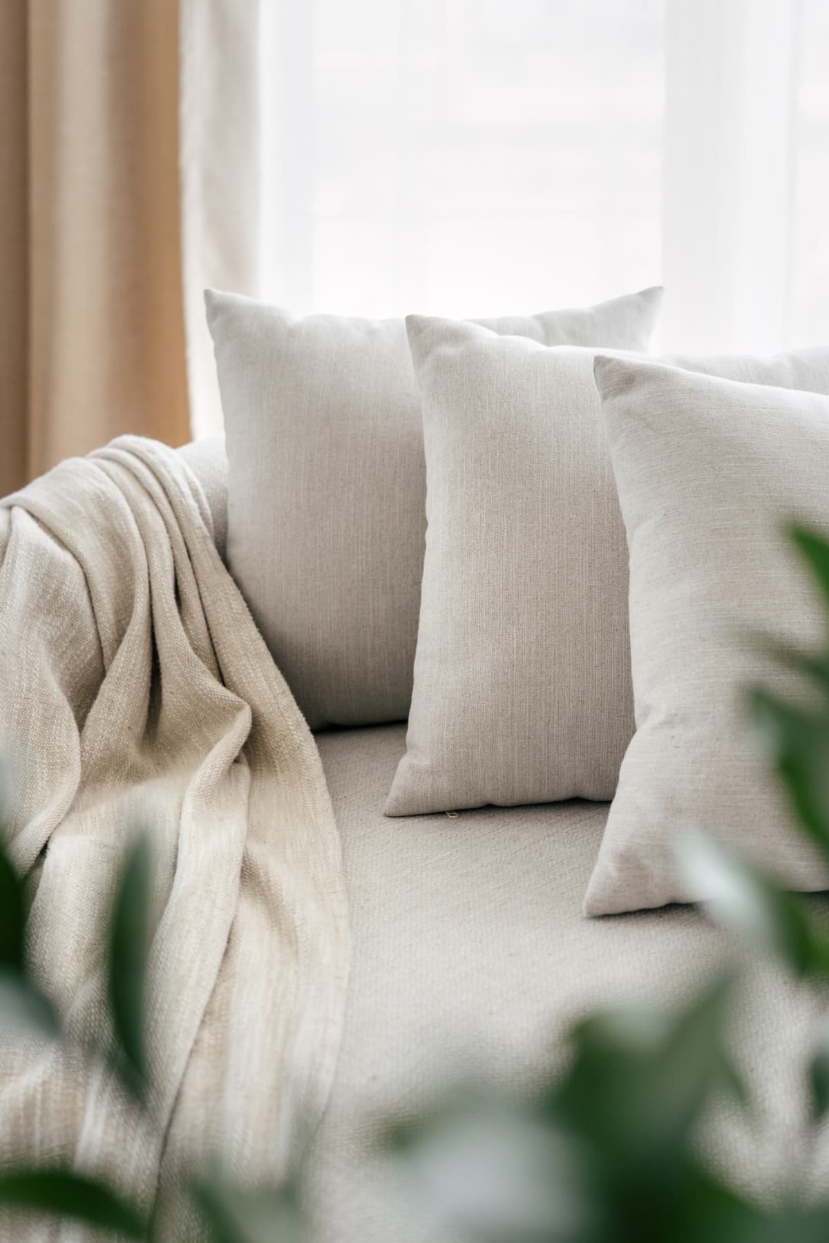 beige couch with three pillows and a blanket