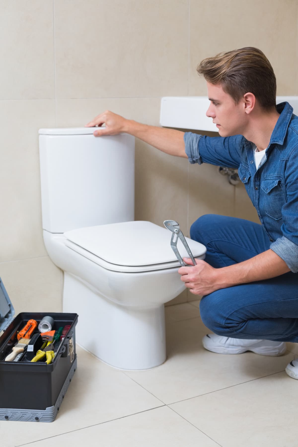 Side view of a plumber with toolbox doing toilet reparation