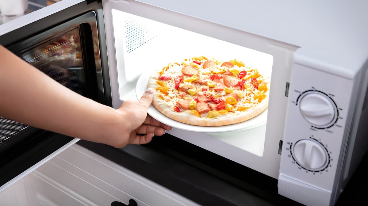 Hand taking a pizzaa out of a microwave