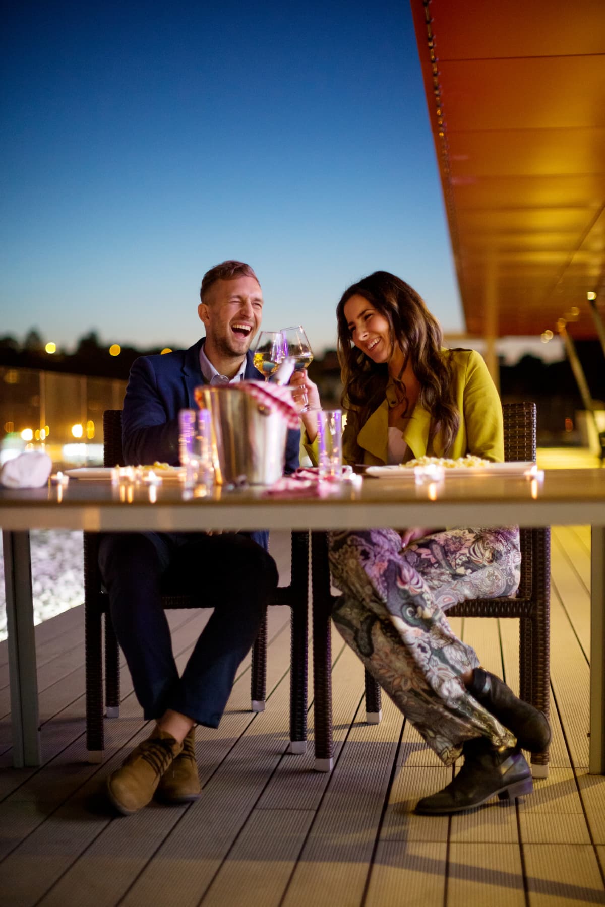 Couple laughing, holding wine in outdoor restaurant at night