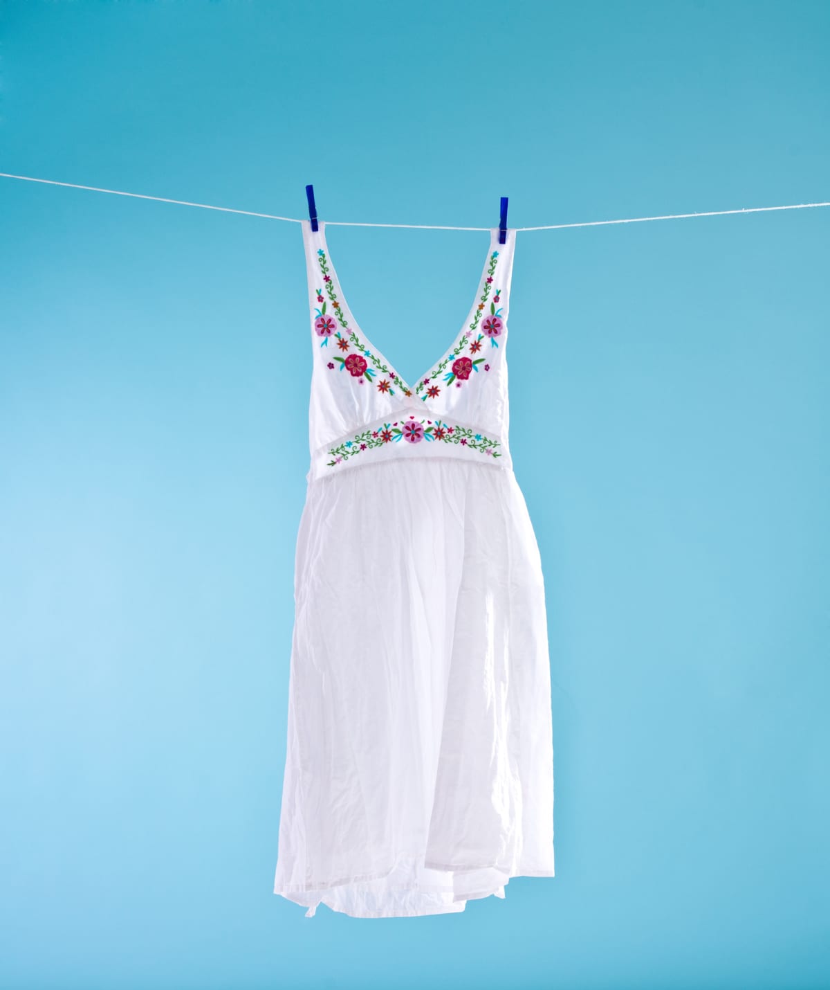 White dress hanging out on a clothesline to dry. Blue background. Summer time.