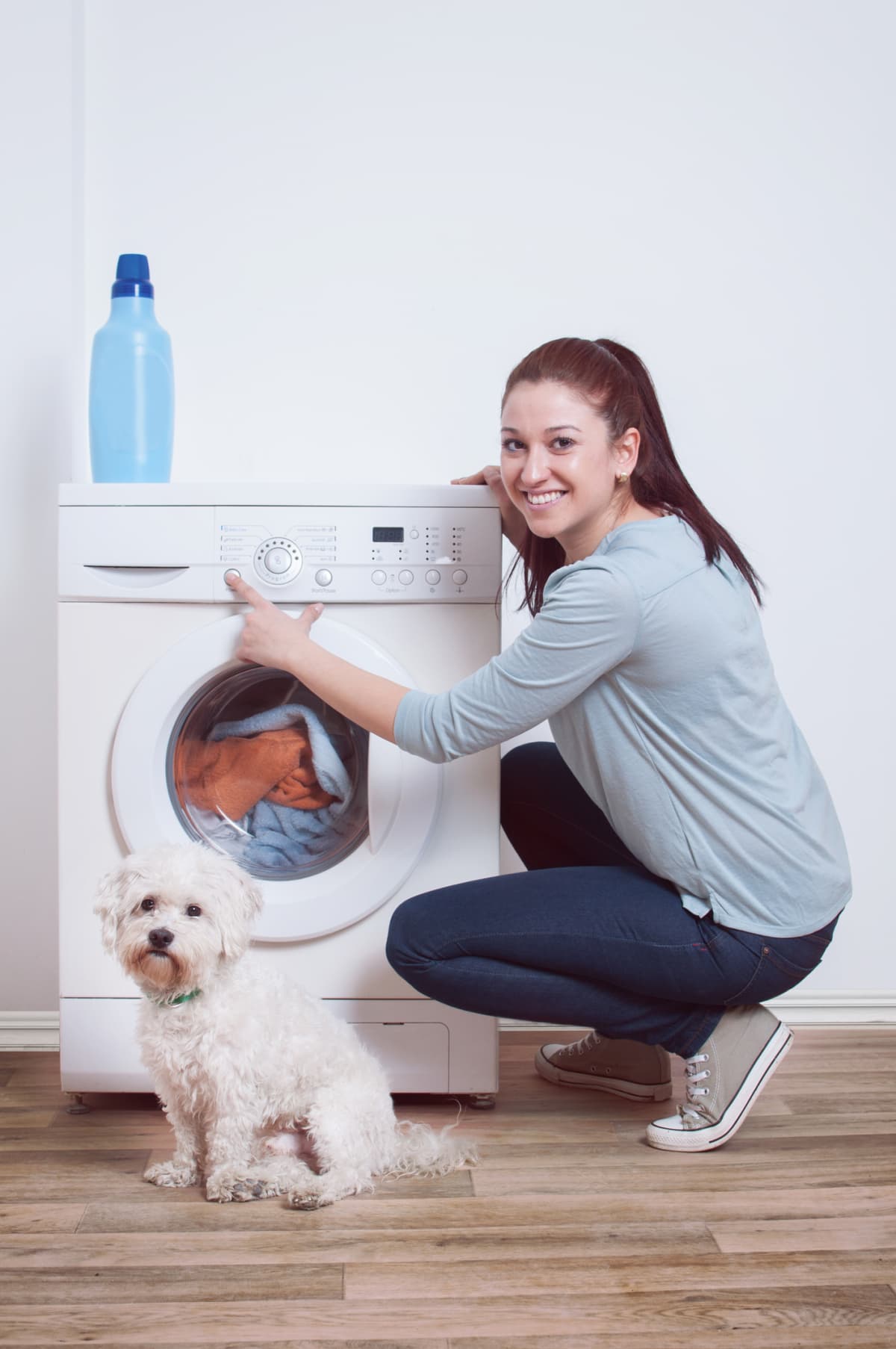 A woman using a washing machine, with her dog sitting nearby