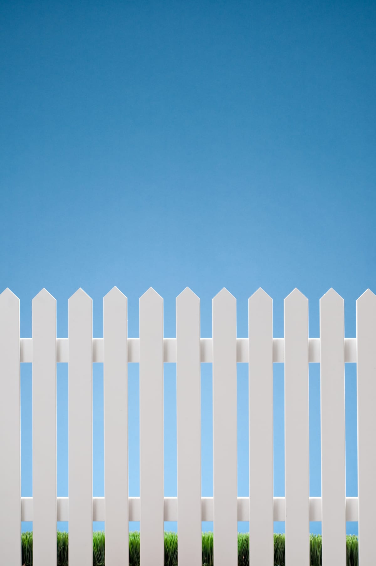 White picket fence against blue sky with grass in the bottom. Shot in the studio.