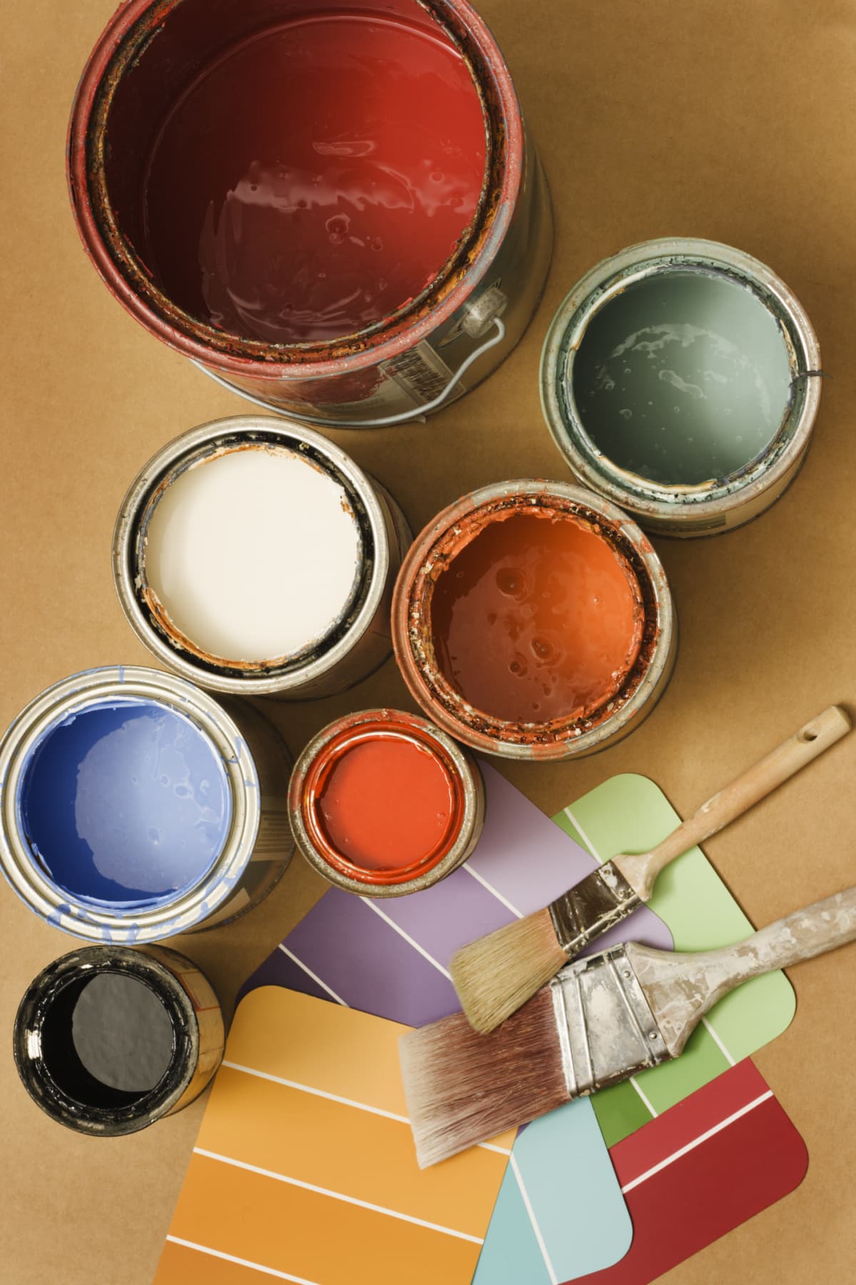 Open paint cans, paintbrushes and color swatches in preparation for home decorating and home improvement painting projects. Some containers are old, with crusted latex paint on bucket edges. Color coordination choices may create decor ideas. Vertical format still life of group of objects, viewed from directly above, with no people.