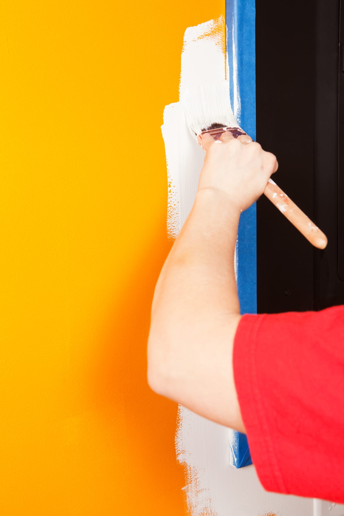 Close up view of a person painting over painter's tape using a paint brush