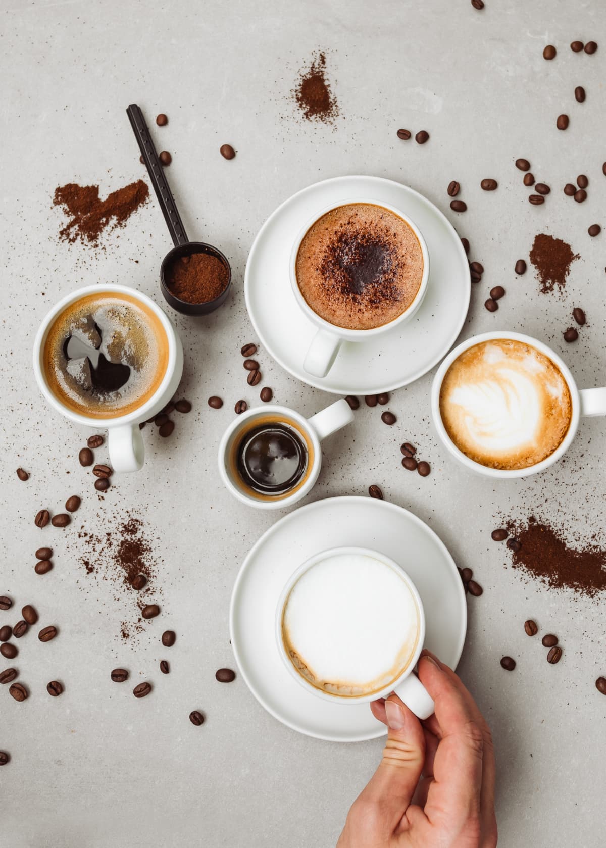 Cropped hand of person holding coffee cup by scattered coffee beans and cocoa powder on table