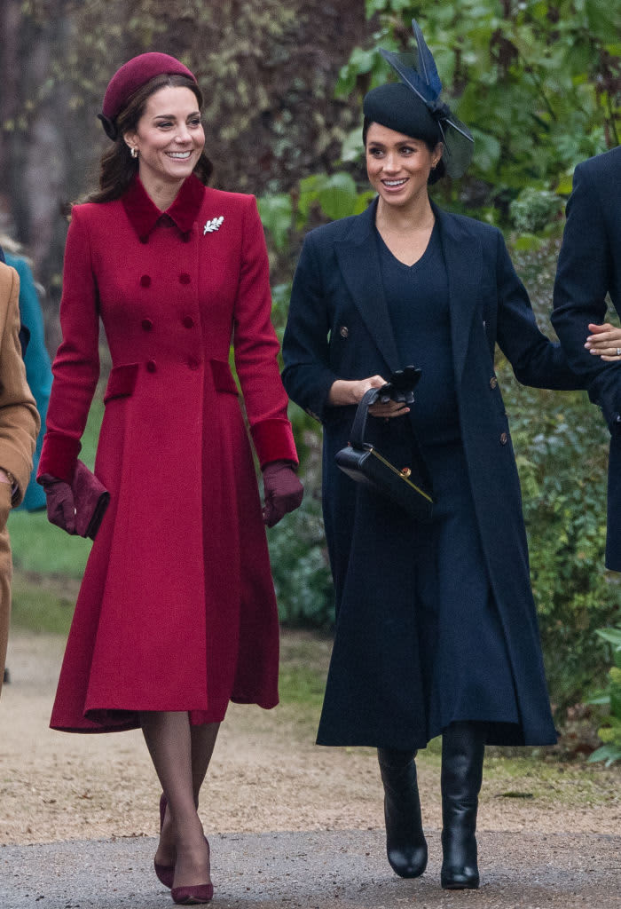 Kate Middleton in red and Meghan Markle in blue walking together and smiling