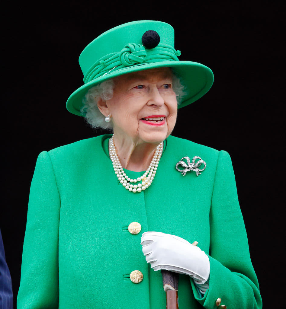 Her Majesty, Queen Elizabeth II in a bright green coat and matching brimmed hat with white gloves, a pearl necklace and earrings and a diamond brooch