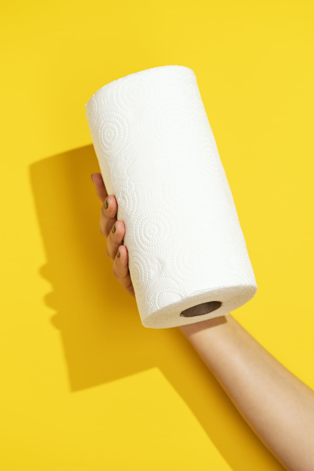 hand holding a roll of paper towels on yellow background