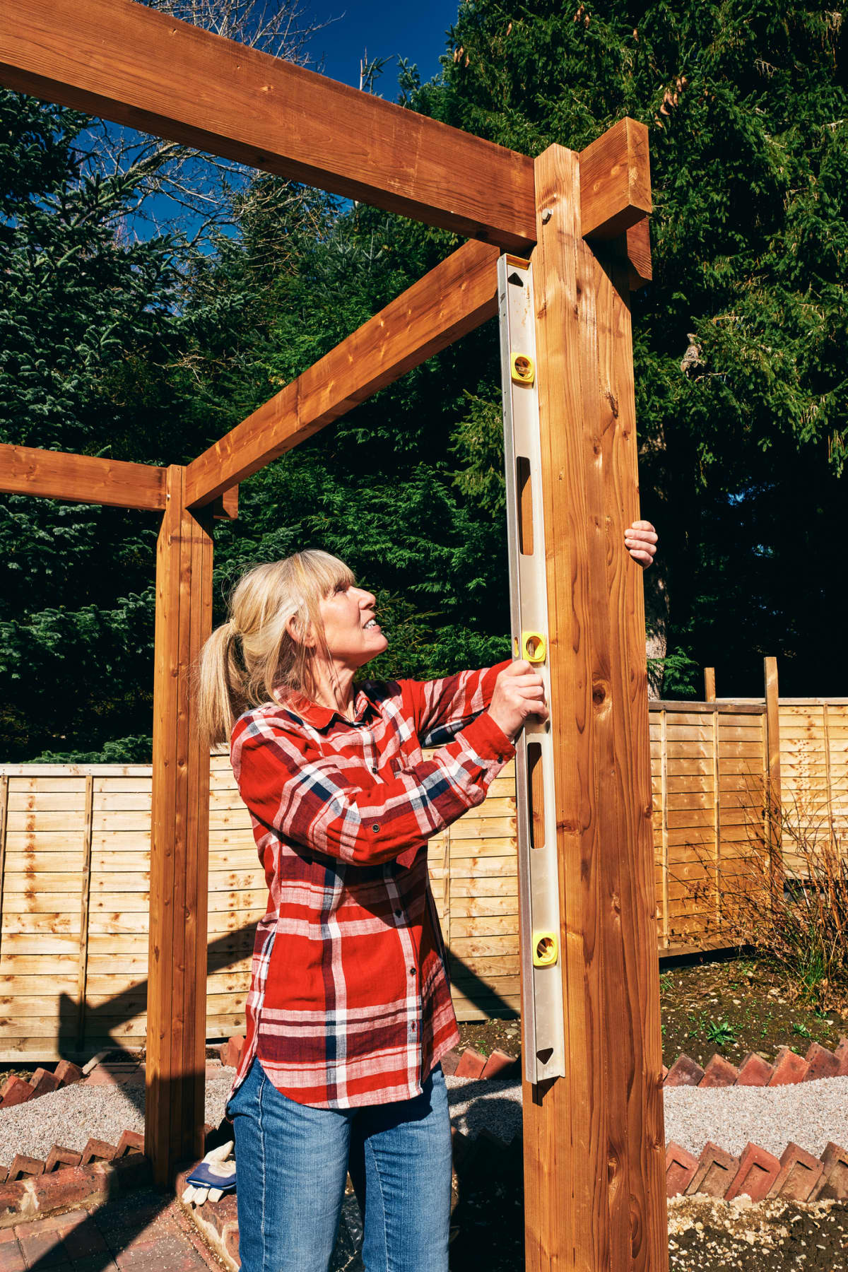 Woman using a spirit level when erecting a wooden pergola in her back yard.