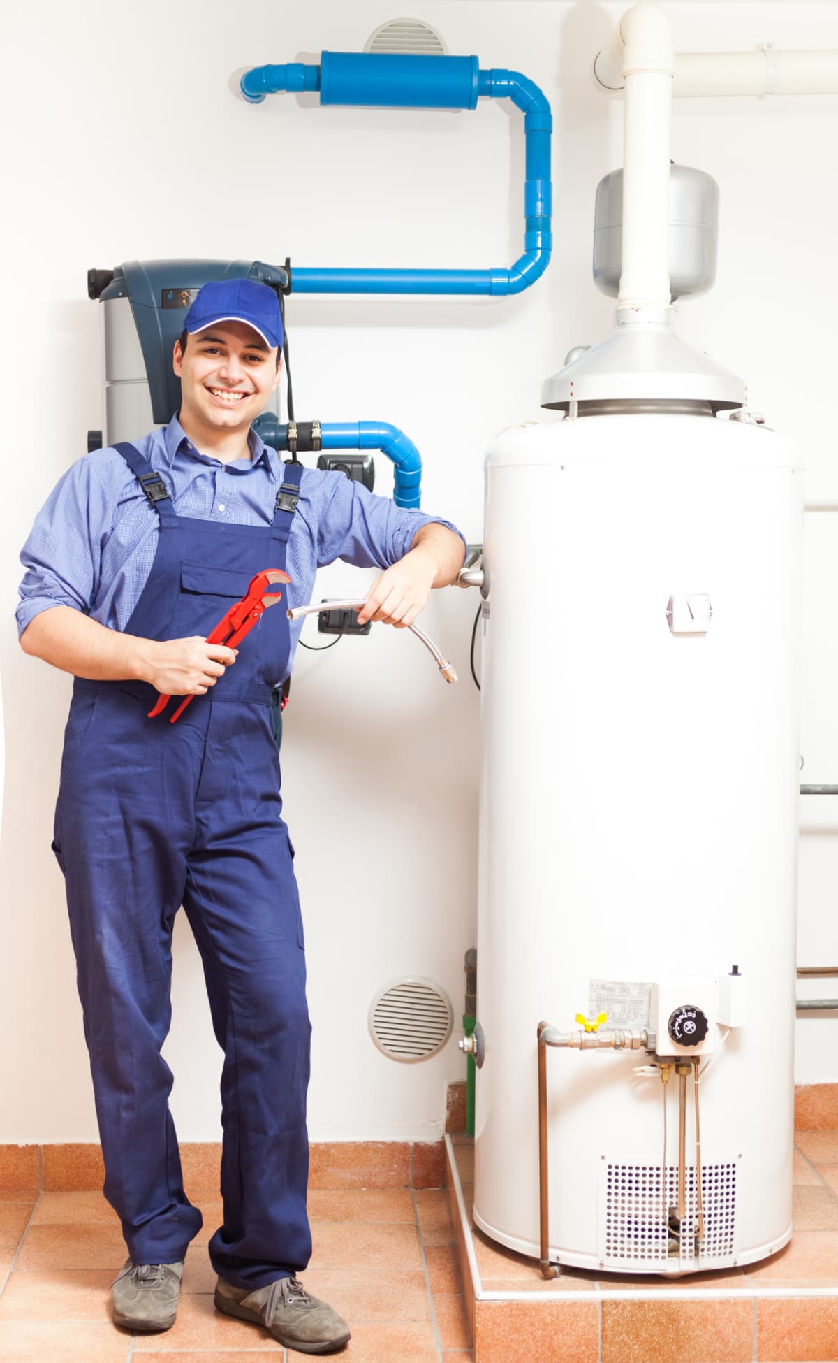 A technician in blue overalls standing by a hot water heater