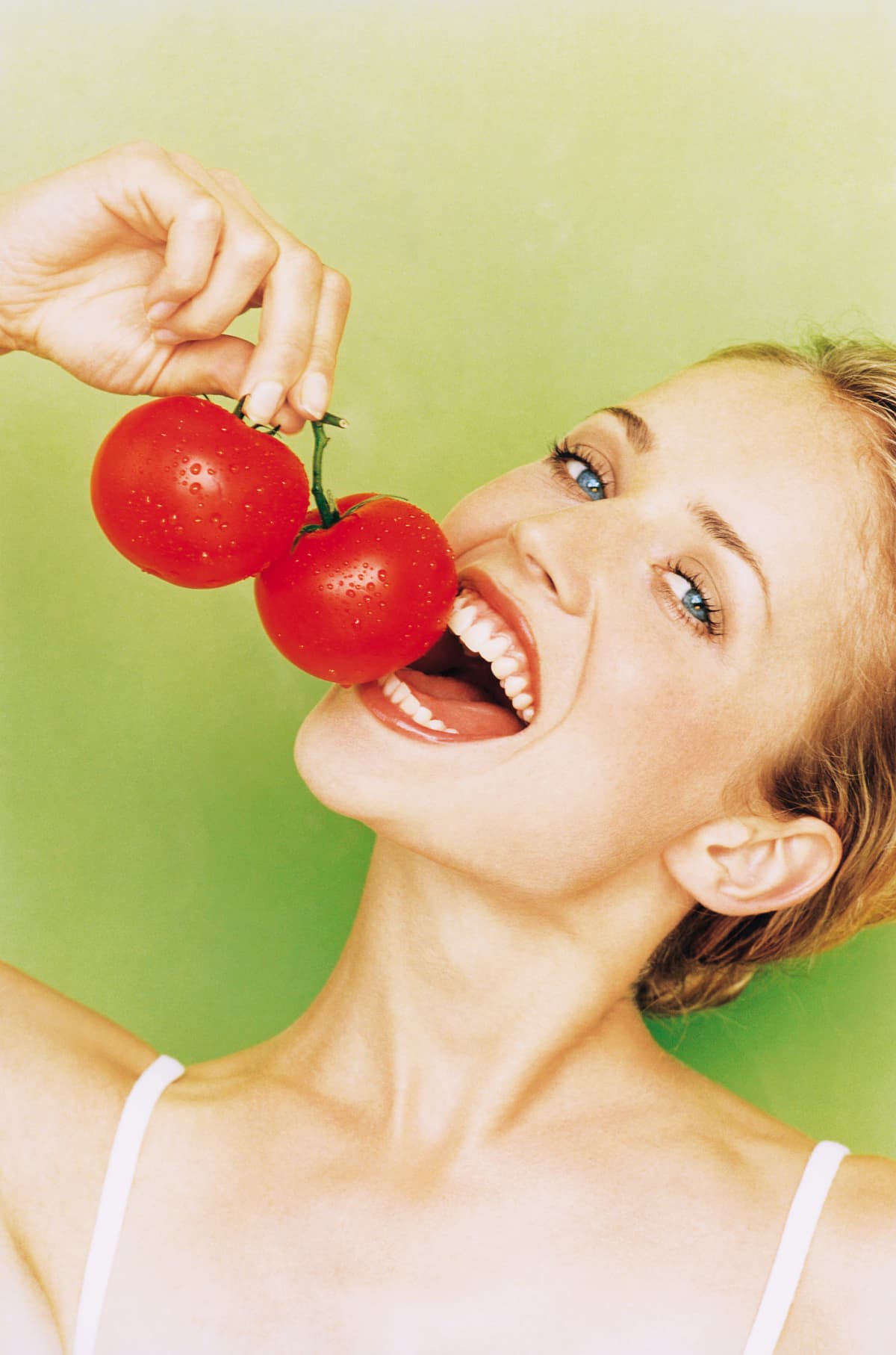 Young smiling woman holding tomatoes up to mouth