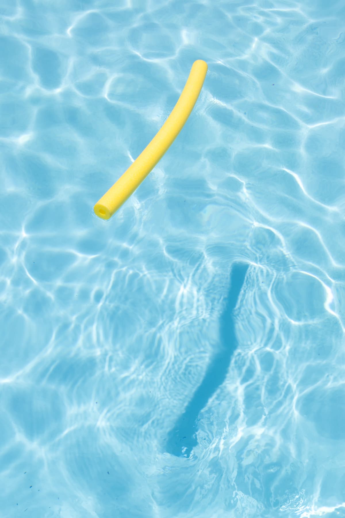 This bright yellow pool noodle is sitting on the surface of clear blue water in a swimming pool.
