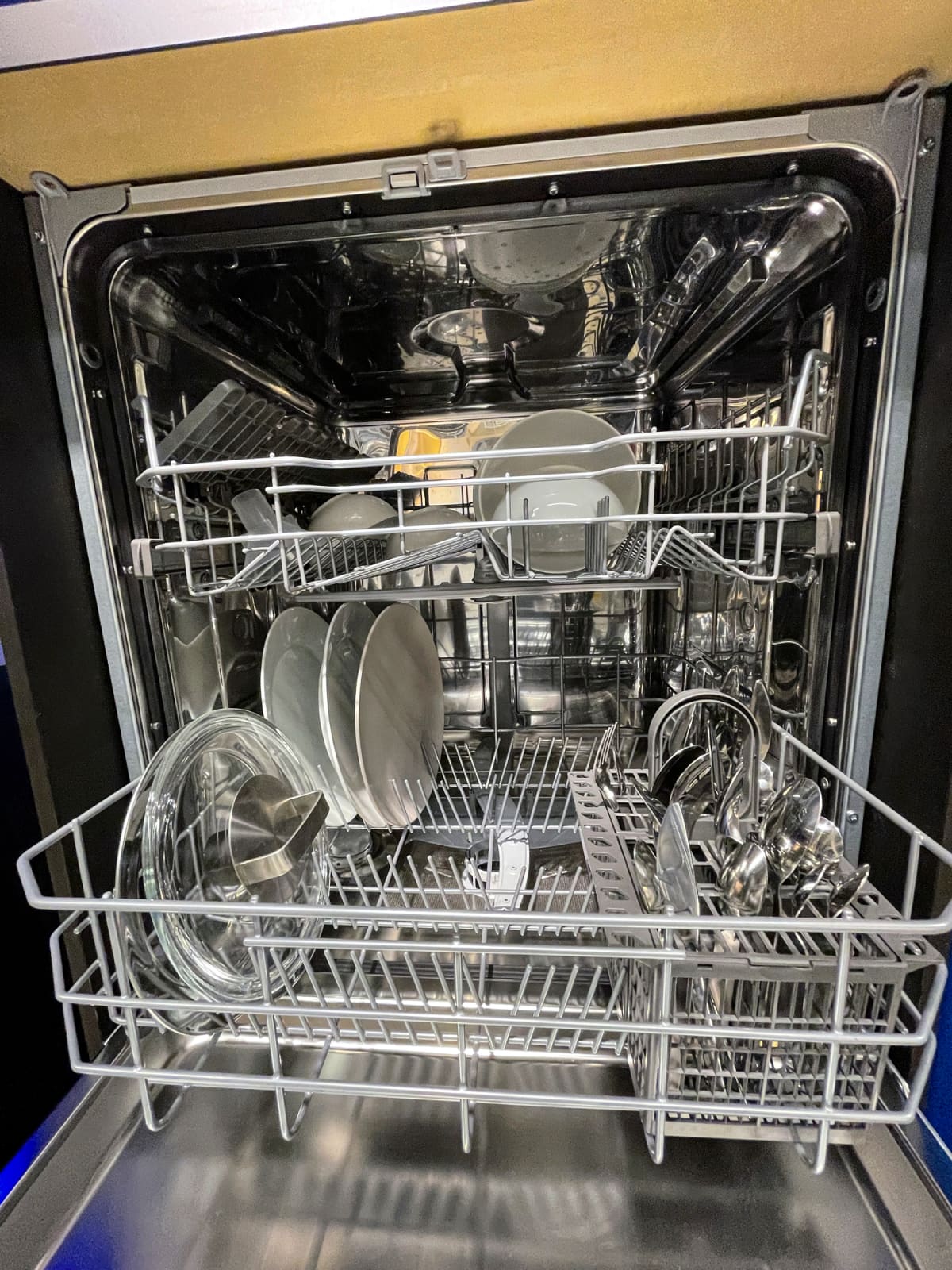 Stock photo showing close-up view of an open dishwasher half loaded with clean cutlery and crockery.