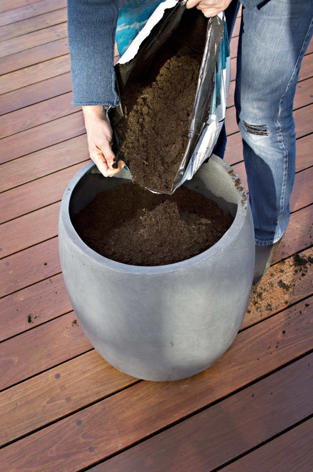 A person pouring potting soil into a container