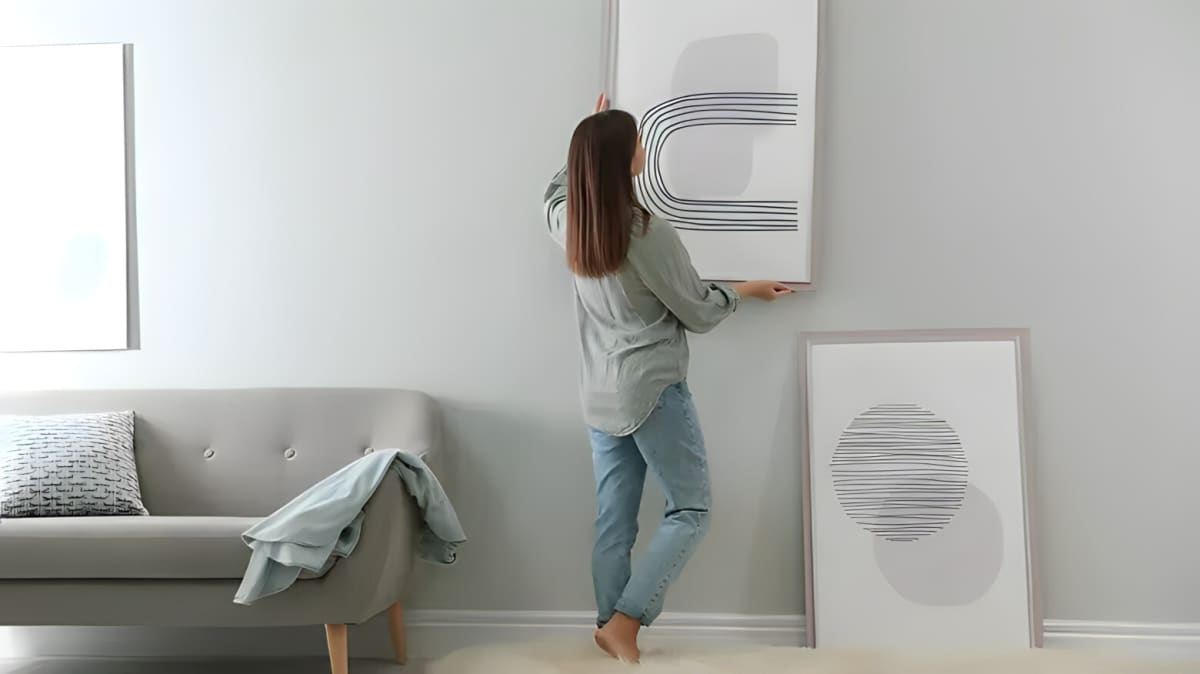 A woman hanging vertical artwork on a wall