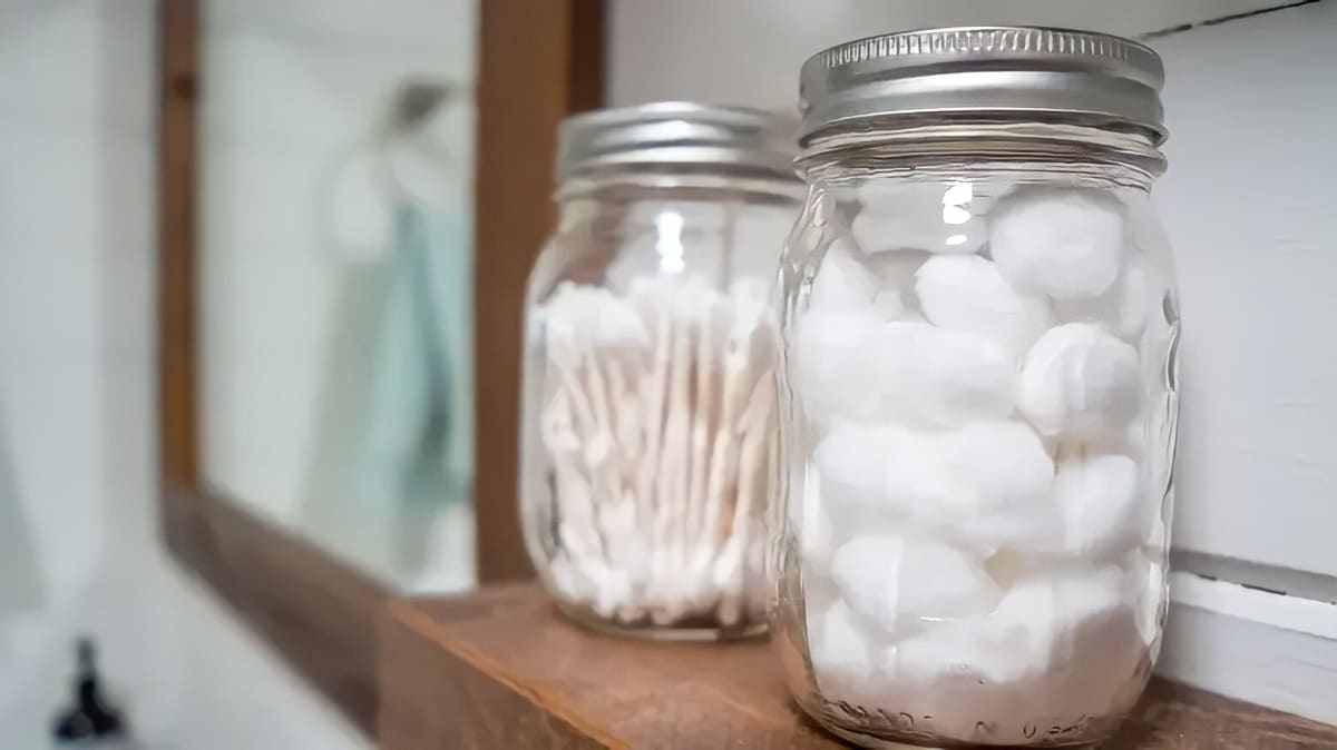 A jar of Q-tips and a jar of cotton balls on a shelf