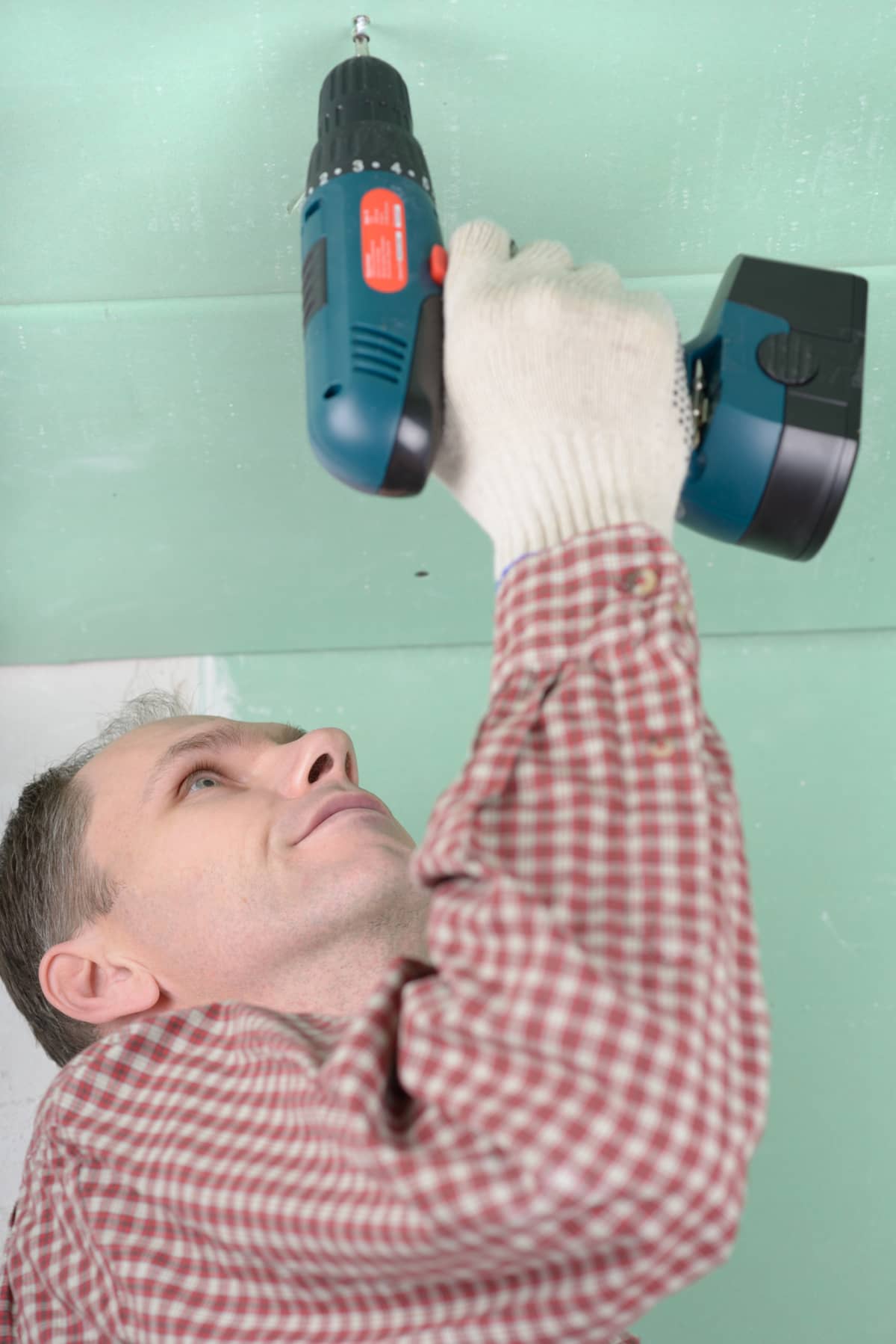 Man installing drywall using cordless drill.