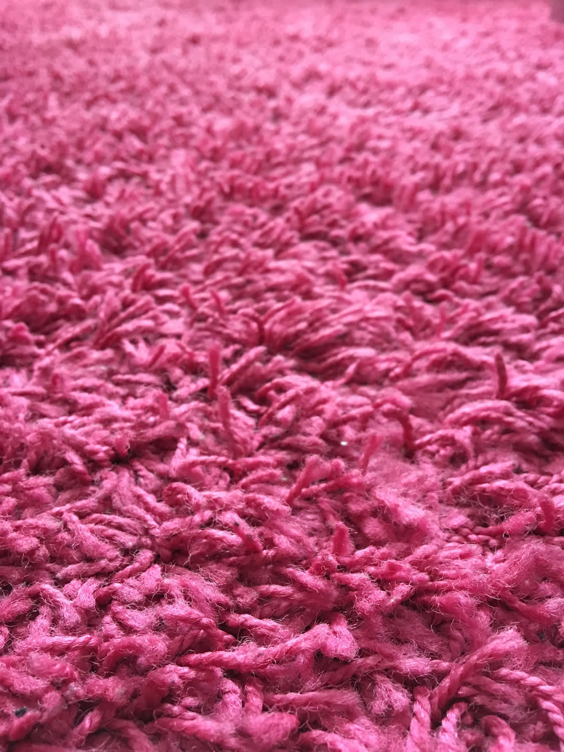 Photo of the pink rug laying on the floor. The rug has a woolly look with long fibres. Fuchsia/magenta colours. Some fluffy bits of the rug sticking out.