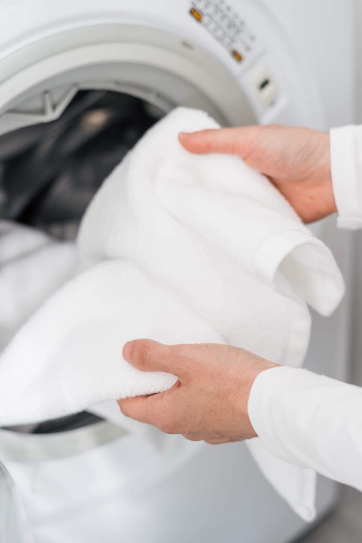 Female hands put white bath towel in automatic washing machine in bathroom in house